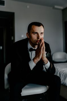 a man in a tuxedo sitting on a chair with his hands folded up