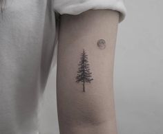 a woman's arm with a pine tree and moon tattoo on the left forearm