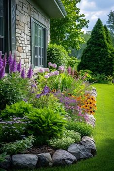 a garden with lots of flowers and rocks in the grass next to a brick building