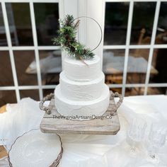 a three tiered white wedding cake with pine cones and evergreen decorations on top, sitting on a wooden platter