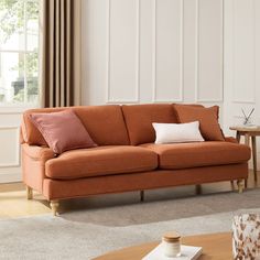 a living room with an orange couch and coffee table in front of the window,