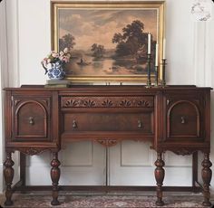 a painting is hanging on the wall above a wooden table with drawers and two vases