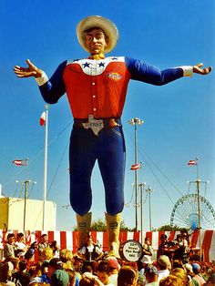 a large statue of a man wearing a cowboy hat is in the middle of a crowd