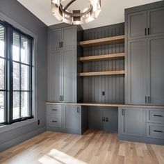 an empty room with wooden floors and gray cabinets, along with a chandelier hanging from the ceiling