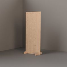 a wooden peg board with holes in it on a gray surface next to a white wall