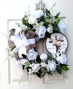 a wreath with white flowers and a cross on the front door is decorated with an ornament