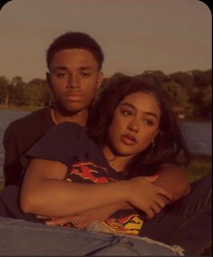 a man and woman sitting next to each other on the grass near a body of water