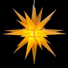 an origami star hanging from a string on a black background with the light turned on