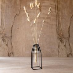 a vase filled with dry grass sitting on top of a wooden table next to a wall