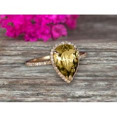 a pear shaped yellow sapphire and diamond ring on top of a wooden table with pink flowers in the background