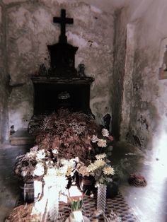 an old church with flowers and candles on the floor in front of a crucifix