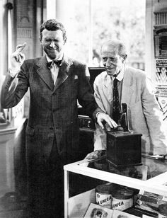 two men standing next to each other in front of a display case with cigars