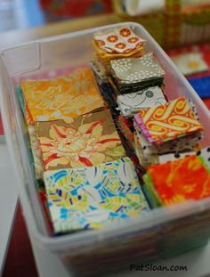 a plastic container filled with lots of different types of colorful paper squares on top of a table