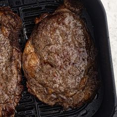 two steaks cooking on top of a grill in a cast iron skillet with tongs