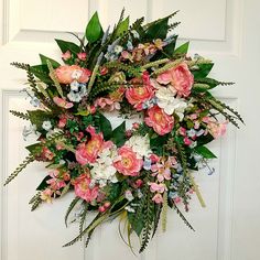 a wreath with pink and white flowers hanging on the front door to greet someone's special occasion