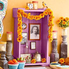 a purple cabinet with flowers and pictures on the wall next to other vases filled with orange flowers