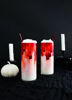 two red and white candles sitting next to each other on a black surface with pumpkins in the background