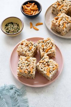 four pieces of rice krispy treats on a pink plate next to bowls of nuts