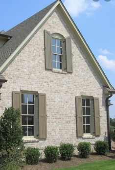 a large brick house with two windows and shutters on the front, along side a green lawn