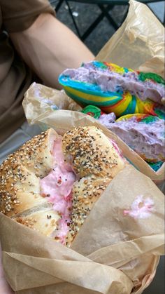 a person holding a bagel with pink frosting and sprinkles