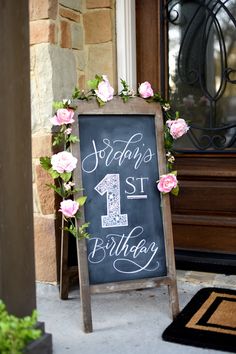 a chalkboard sign that says happy 1st birthday with flowers and greenery on it