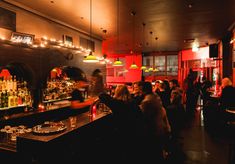 a group of people sitting at a bar in a dimly lit room with red walls