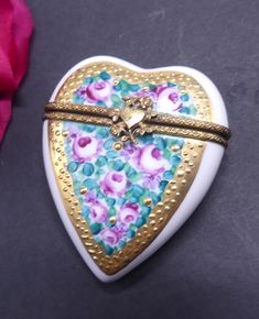 a heart shaped trinket box with flowers on it next to a pink rose