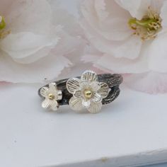 A pretty handmade flower ring based on the Japanese Cherry Blossom in silver and gold. Inspired by Japanese culture and the beautiful cherry blossom, this ring has been hand crafted from sterling silver which has been oxidised to represent the black branches. Cherry blossom has long been symbolic of celebrations and the cycle of life, making this a perfect treat for yourself or a special gift for loved ones. Set with silver blossom with solid gold centres this is a special ring to treasure. Matc Nature-inspired Adjustable Flower Ring For Anniversary, Flower Shaped Hand Forged Jewelry Gift, Hand Forged Flower Jewelry Gift, Hand Forged Flower Shaped Jewelry Gift, Nature-inspired White Gold Promise Jewelry, White Gold Nature-inspired Jewelry For Promise, Nature-inspired Stackable Jewelry For Anniversary, Nature-inspired Stackable Jewelry For Anniversaries, Nature-inspired Nickel Free Anniversary Ring