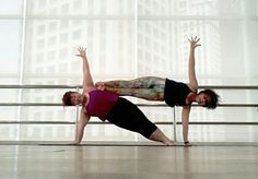 two women doing yoga poses in front of a large window with their arms stretched out