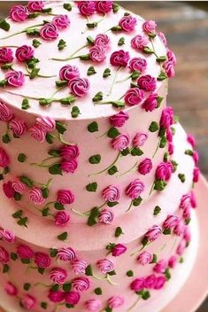 a three tiered cake with pink frosting and roses on it's side