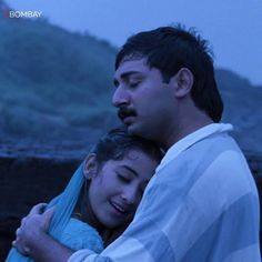 a man and woman embracing each other in front of a hill with the sky behind them