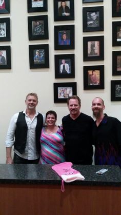 three men and a woman standing in front of a counter with pictures on the wall behind them