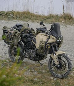 a motorcycle parked on the side of a dirt road next to some grass and bushes