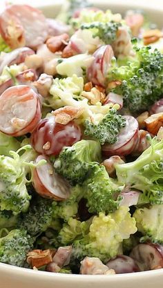 a salad with broccoli, grapes and nuts in a white bowl on a table