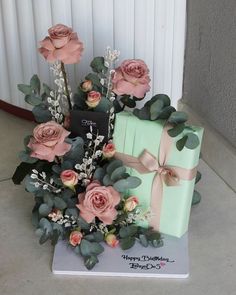 a birthday cake with roses and greenery on it, sitting next to a gift box