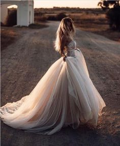 a woman in a wedding dress standing on a dirt road with her back to the camera