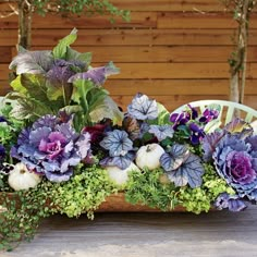 a basket filled with purple flowers sitting on top of a wooden table next to pumpkins