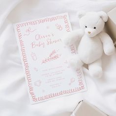 a white teddy bear sitting next to a baby shower book on top of a bed