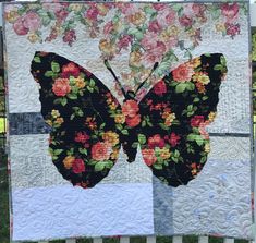 a quilted butterfly with flowers on it's wings is hanging from a fence