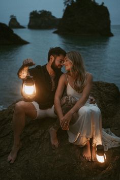 a man and woman sitting on top of a rock next to each other holding lanterns