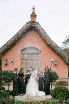 a bride and her bridal party in front of a pink building with fountain spraying water