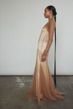 a woman standing in front of a white wall wearing a beige dress and holding a black pole