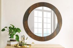 a round mirror sitting on top of a wooden table next to a potted plant