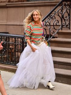 a woman is walking down the street wearing a white tulle skirt and striped shirt