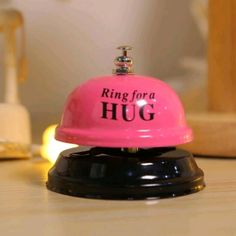 a pink bell with the words ring for a hug on it sitting on a table