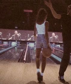 two people standing in front of a bowling alley with bowling balls on the floor and one person holding a basketball