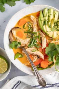 a white bowl filled with chicken, avocado and carrots next to a spoon