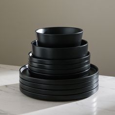 stack of black plates sitting on top of a white counter next to a gray wall