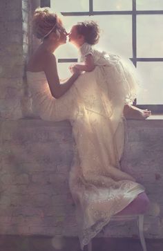 two women in white dresses are kissing each other by a window with the sun shining through