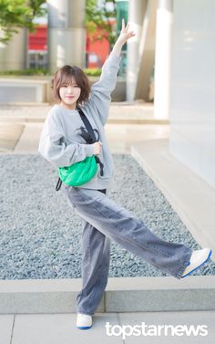 a young woman is posing for the camera with her hand up in the air while wearing grey sweatpants and a green backpack